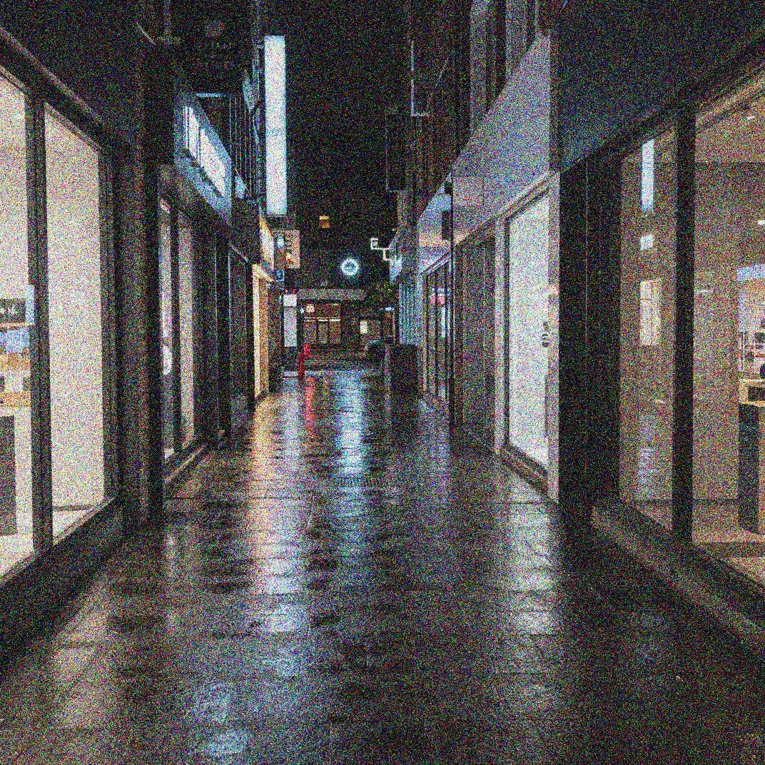 Grainy iPhone night photo of a city street with speckled shadows and noisy sky before AI noise reduction